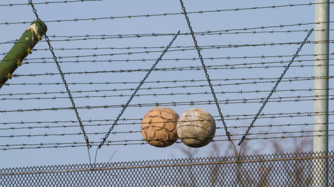 Two soccer balls caught in the top of a barbed wire prison fence